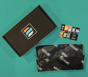 Dipixion packaging on a bright blue background. Our sleek, branded black box. Colourful thank you card, and tissue paper wrapped t-shirts.